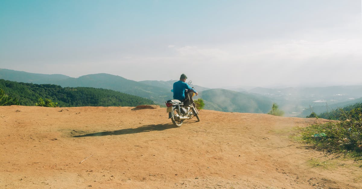 A motorcyclist admires the breathtaking mountain landscape from a dirt path.
