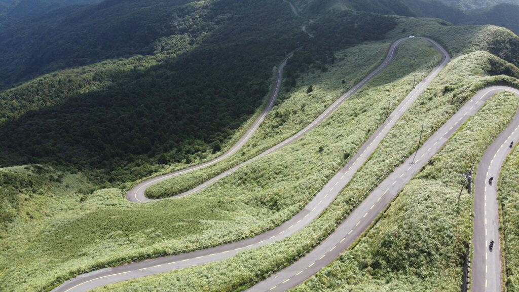The Nan Loop: Thailand's Most Underrated Motorcycle Route Aerial view of a winding mountain road surrounded by lush green forest in Ruifang District, Taiwan.