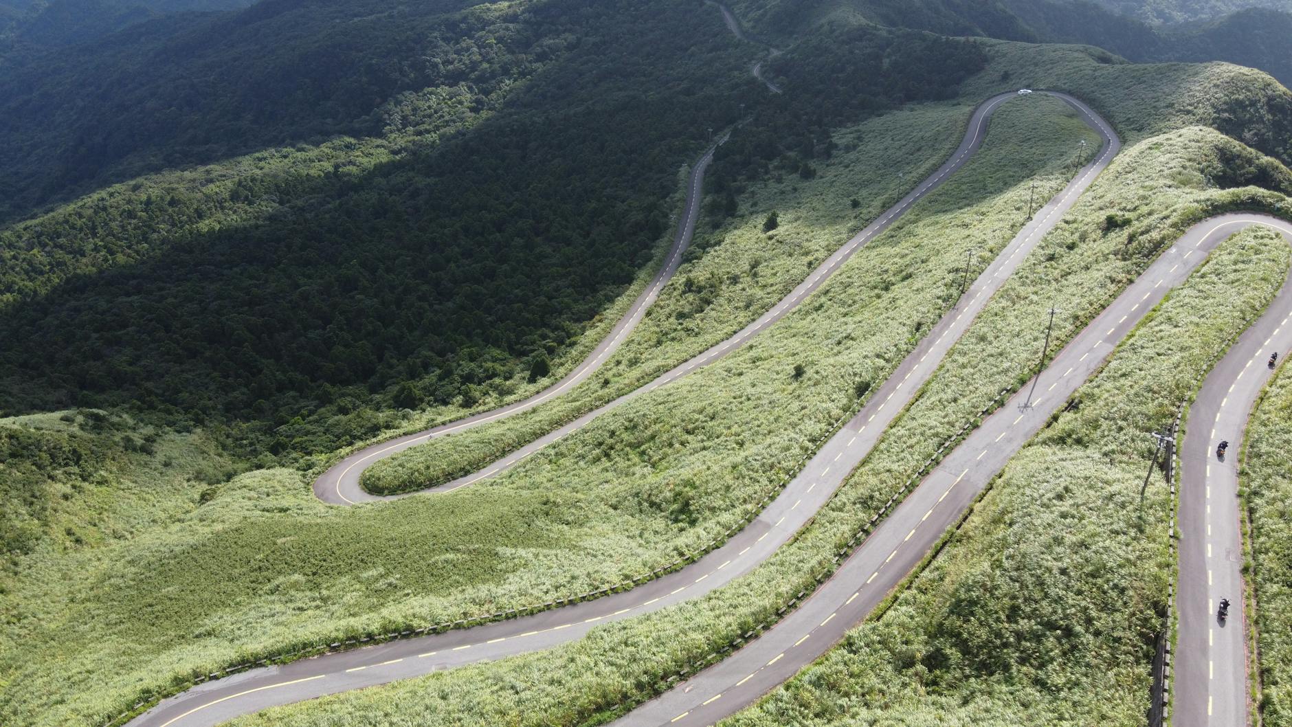Aerial view of a winding mountain road surrounded by lush green forest in Ruifang District, Taiwan.