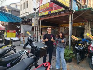 Thai Man and Woman standing outside motorbike rental shop showing thumbs up