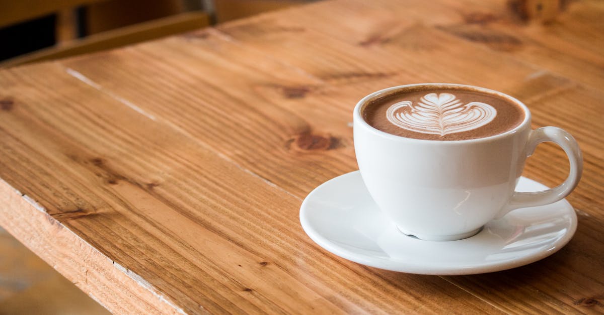 Best coffee shops in Krabi with stunning views Close-up of a white cup of latte with artistic foam on a rustic wooden table.